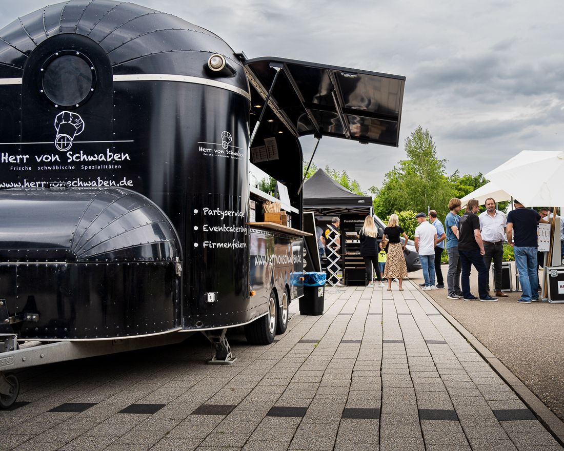Geöffneter schwarzer Foodtrailer von Herr von Schwaben auf einer gepflasterten Fläche, Gäste warten auf die Ausgabe