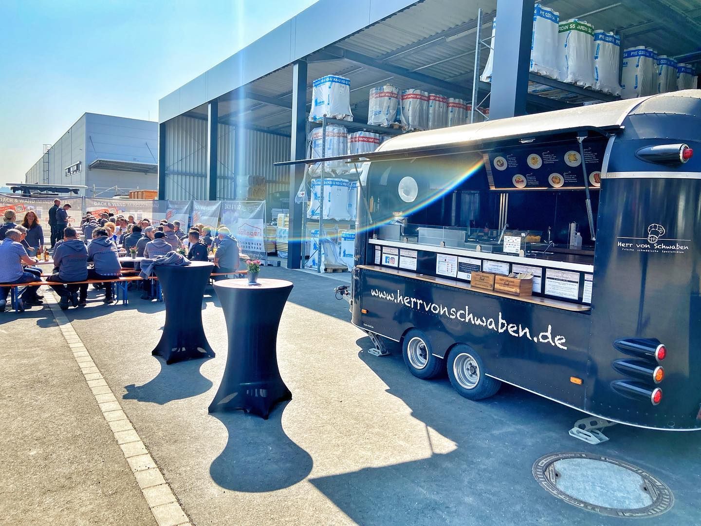 Foodtrailer von Herr von Schwaben auf dem Firmengelände, Mitarbeiter essen an Biertischen